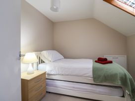 A single bed with white bedding and a green throw in a small attic bedroom with a wooden bedside table and lamp at Woodstock in Chaffcombe near Chard