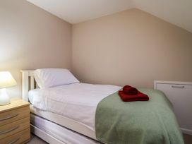 A bedroom with a single bed with white sheets and green cover with red towels on top and a nightstand with a lamp at Woodstock in Chaffcombe near Chard