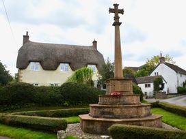 A war memorial cross surrounded by trimmed hedges with thatched and white houses in the background in Woodstock Chaffcombe near Chard