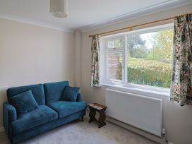 A room with a blue sofa a small wooden side table a window with floral curtains and a radiator below the window at Woodstock in Chaffcombe near Chard