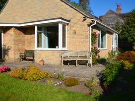 An outdoor patio area with benches and flower beds beside a stone house at Woodstock in Chaffcombe near Chard