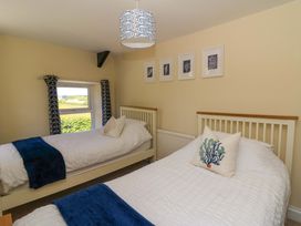 A bedroom with two single beds white bedding blue throws and a window with patterned curtains at Towyn Hall in New Quay