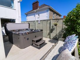 An outdoor patio area with a hot tub and a cushioned bench with blue and white pillows at Towyn Hall in New Quay