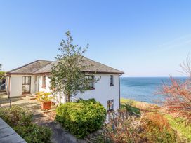 A white house with a pitched roof surrounded by shrubs and trees near the sea at Gwylanod in Llwyngwril near Fairbourne