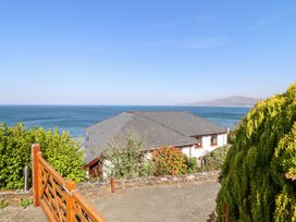 A house with a pitched roof by the sea with a wooden gate and greenery at Gwylanod in Llwyngwril near Fairbourne