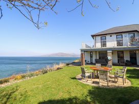 A house with a patio set on a grassy lawn overlooking the sea at Gwylanod in Llwyngwril near Fairbourne