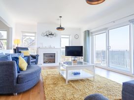 A living room with sofas, a coffee table, a television, a fireplace, and large windows at Gwylanod in Llwyngwril near Fairbourne