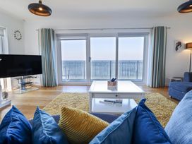 A living room with blue and yellow cushions on a sofa a white coffee table a yellow rug a television and glass doors leading to a balcony overlooking the sea at Gwylanod in Llwyngwril near Fairbourne