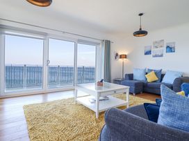 A living room with sofa and cushions a coffee table and sliding glass doors overlooking the sea at Gwylanod in Llwyngwril near Fairbourne