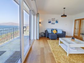 A living room with a blue sofa and yellow rug next to sliding glass doors overlooking water at Gwylanod in Llwyngwril near Fairbourne
