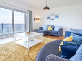 A living room with blue sofas yellow cushions white coffee table and large windows overlooking the sea at Gwylanod in Llwyngwril near Fairbourne