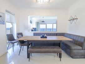 A dining area with a wooden table surrounded by a bench and chairs with a large mirror reflecting a window overlooking the sea at Gwylanod in Llwyngwril near Fairbourne