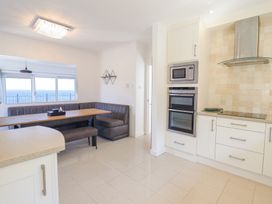 A kitchen with an oven, microwave, and a seating area with a wooden table and corner bench at Gwylanod in Llwyngwril near Fairbourne