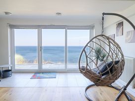 A room with a hanging chair a small table a plant and large sliding glass doors showing an ocean view at Gwylanod in Llwyngwril near Fairbourne