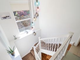 A stairway with brown carpet and white railing with a window and hanging pendant lights at Gwylanod in Llwyngwril near Fairbourne
