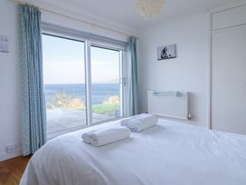 A bedroom with a bed towel on it overlooking the sea through sliding glass doors at Gwylanod in Llwyngwril near Fairbourne