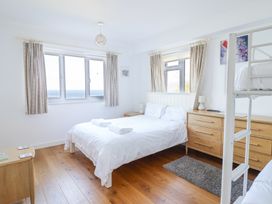 A bedroom with a double bed with white bedding a bunk bed wooden dressers and windows with curtains at Gwylanod in Llwyngwril near Fairbourne