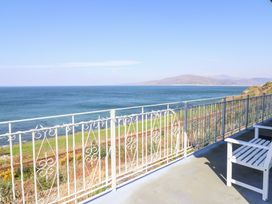 A balcony with white railing and chair overlooking the sea and distant hills at Gwylanod in Llwyngwril near Fairbourne