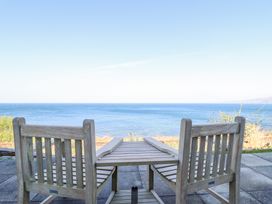 An outdoor seating area with two wooden chairs and a table overlooking the sea at Gwylanod in Llwyngwril near Fairbourne