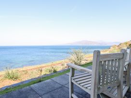 Wooden chairs on a paved patio facing the sea with railway tracks and hills in the background at Gwylanod in Llwyngwril near Fairbourne