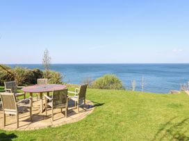 A patio area with a round wooden table and six chairs on a stone floor overlooking the sea at Gwylanod in Llwyngwril near Fairbourne