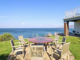 A circular wooden table with six wooden chairs on a patio overlooking the sea at Gwylanod in Llwyngwril near Fairbourne