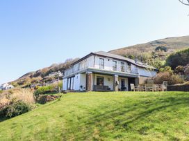 A two-story house with a balcony and outdoor seating on a grassy hill at Gwylanod in Llwyngwril near Fairbourne
