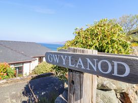 A wooden signpost with the word Gwylanod near buildings and greenery with a view of the sea at Gwylanod Llwyngwril near Fairbourne