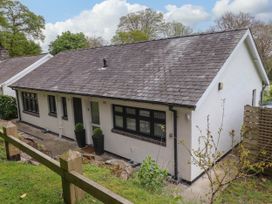 A single story house with a sloped roof and multiple windows surrounded by trees at Glyn-Y-Mor in Llanbedrog