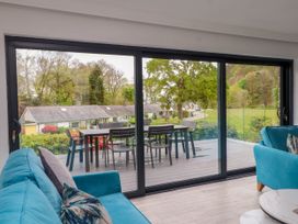 A living room with blue sofas and pillows facing a glass sliding door opening to a deck with a table and chairs at Glyn-Y-Mor in Llanbedrog