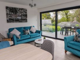 A living room with blue sofas and a dining table near large glass doors overlooking a patio at Glyn-Y-Mor in Llanbedrog
