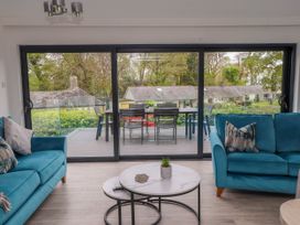 A living room with two blue sofas and round coffee tables facing a sliding glass door at Glyn-Y-Mor in Llanbedrog