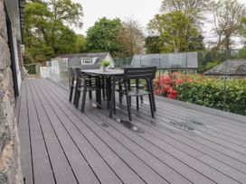 An outdoor deck with a black dining table and chairs surrounded by glass railing and greenery at Glyn-Y-Mor in Llanbedrog