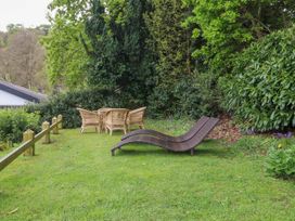 An outdoor garden area with two wicker loungers and a round table with four wicker chairs surrounded by trees and bushes at Glyn-Y-Mor in Llanbedrog