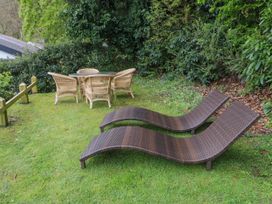 An outdoor area with two brown lounge chairs and a round table with four wicker chairs on grass at Glyn-Y-Mor in Llanbedrog