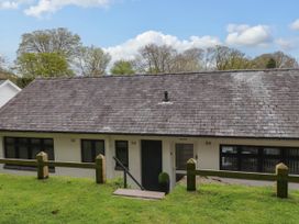 A single story house with a sloped roof and front door surrounded by grass and wooden fencing at Glyn-Y-Mor in Llanbedrog
