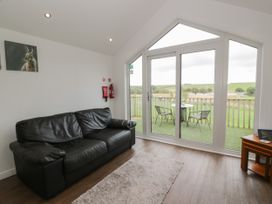 A living room with a black leather sofa a rug and glass doors opening to a balcony with chairs and a table at Mallard Lodge in Moscow near Galston