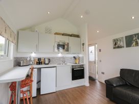 A kitchen area with white cabinets a microwave and oven a small fridge a toaster and kettle with a black leather sofa and paintings on the wall at Mallard Lodge in Moscow near Galston