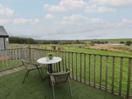 A balcony with two chairs and a round table overlooking a grassy field with trees and a pond at Mallard Lodge in Moscow near Galston