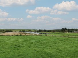 A grassy field with a pond and trees under a cloudy sky at Mallard Lodge in Moscow near Galston