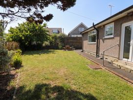 A garden with grass and a wooden bench at Llwyn Eithin in Benllech