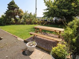 A garden with a wooden bench and flower pots at Llwyn Eithin in Benllech