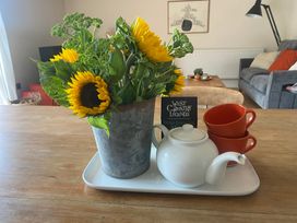 A tray with sunflowers in a pot, a teapot, red cups and a book in a living room at Church Farm Dairy Cadbury near Thorverton