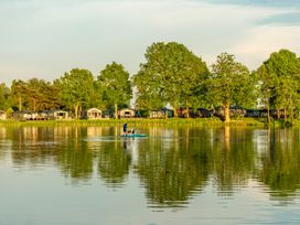 A person on a paddleboard on a lake near cabins and trees at Heron in Shobdon