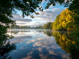 A lake surrounded by trees and blue sky at Heron in Shobdon