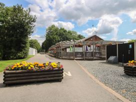 An outdoor seating area with hanging flower baskets near a building with a sign that reads Lakeside Bar Bistro in a park setting at Owl in Shobdon