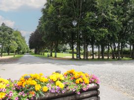 A park with a pathway lined by trees and a flower bed with yellow and purple flowers at Owl in Shobdon