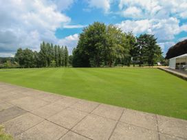 A large green lawn with a paved walkway and trees in the background at Owl in Shobdon