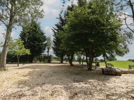 An outdoor play area with wood chips ground covering trees benches and playground equipment at Owl in Shobdon