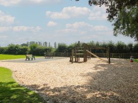 An outdoor playground with a slide and swing surrounded by wood chips and benches at Owl in Shobdon